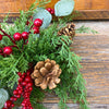 Decorative arrangement of greenery, red berries, and pine cones on a wooden surface. Berry and Cedar Dripping Floral Orbs - Two Styles available at Quilted Cabin Home Decor.