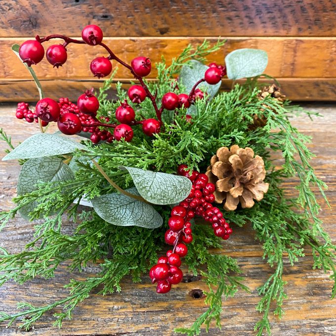 Decorative arrangement of red berries, green foliage, and pine cones on a wooden surface. Berry and Cedar Dripping Floral Orbs - Two Styles available at Quilted Cabin Home Decor.