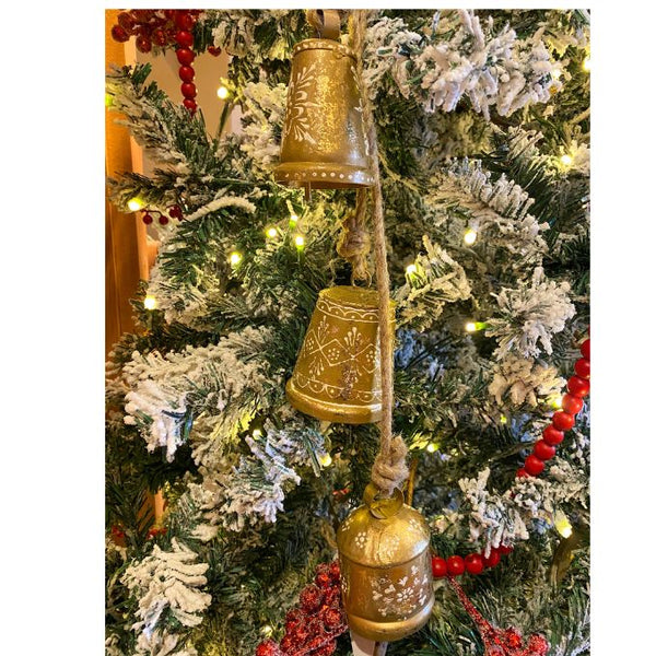 Decorative gold bells hanging on a Christmas tree with lights and red berries. Gold Henna Painted Bell Cluster available at Quilted Cabin Home Decor.