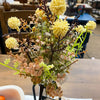 Bouquet of artificial flowers with yellow and green elements on a wooden surface. Cream Pincushion Floral Spray available at Quilted Cabin Home Decor.