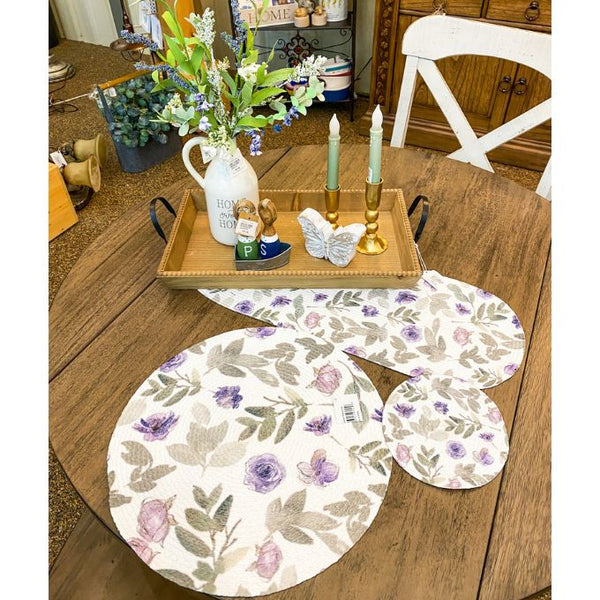 Floral-patterned placemats on a wooden table with decorative items. Violet Meadow Table Linen Collection - Three Styles available at Quilted Cabin Home Decor.