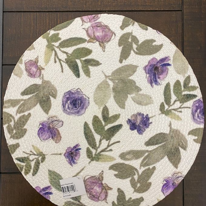 Round floral mat with purple flowers and green leaves on a wooden surface. Violet Meadow Table Linen Collection - Three Styles available at Quilted Cabin Home Decor.