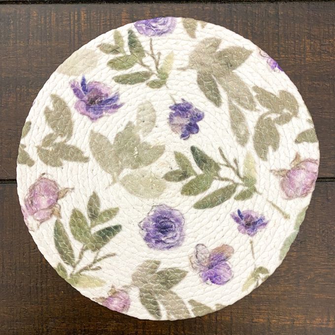 Round floral placemat with purple and green flowers on a wooden surface. Violet Meadow Table Linen Collection - Three Styles available at Quilted Cabin Home Decor.