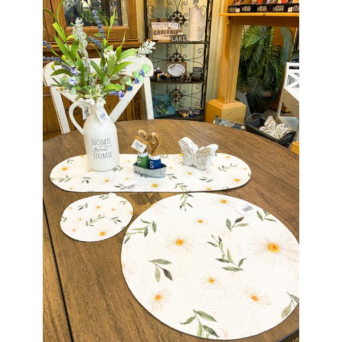 Round floral placemats on a wooden table with decorative items. Daisy Blossom Braided Table Linens - Three Styles available at Quilted Cabin Home Decor.