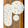 Set of three round placemats with floral pattern on a wooden surface. Daisy Blossom Braided Table Linens - Three Styles available at Quilted Cabin Home Decor.