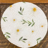 Round woven trivet with floral patterns on a wooden surface. Daisy Blossom Braided Table Linens - Three Styles available at Quilted Cabin Home Decor.