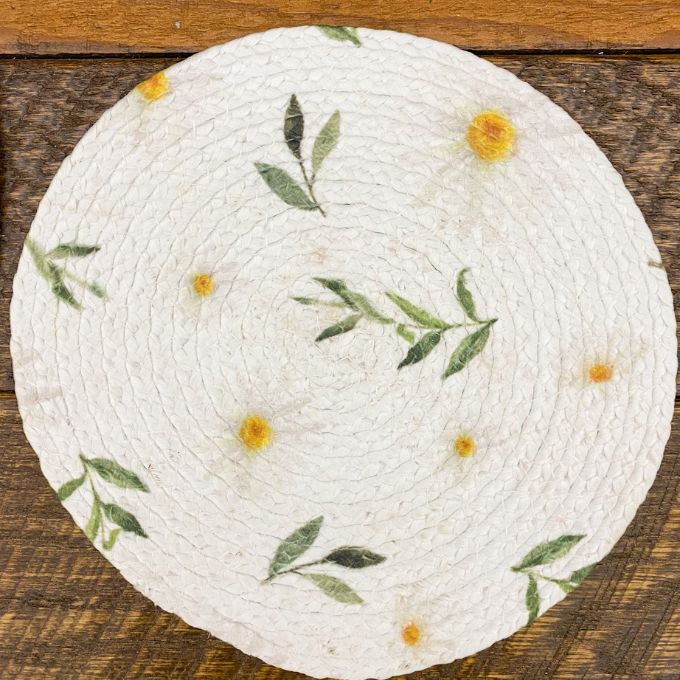 Round woven trivet with floral patterns on a wooden surface. Daisy Blossom Braided Table Linens - Three Styles available at Quilted Cabin Home Decor.