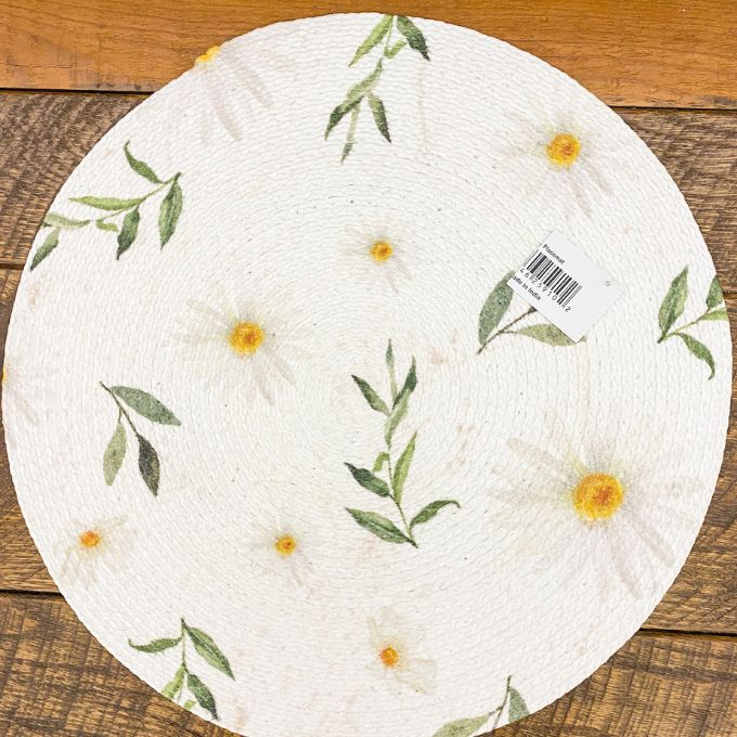 Round paper placemat with floral design on a wooden surface. Daisy Blossom Braided Table Linens - Three Styles available at Quilted Cabin Home Decor.