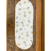 Oval-shaped table runner with floral pattern on a wooden background. Daisy Blossom Braided Table Linens - Three Styles available at Quilted Cabin Home Decor.
