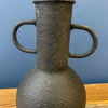 Textured vase with two handles on a wooden surface and blue background. Rustic Metal Vases - Two Colours available at Quilted Cabin Home Decor.