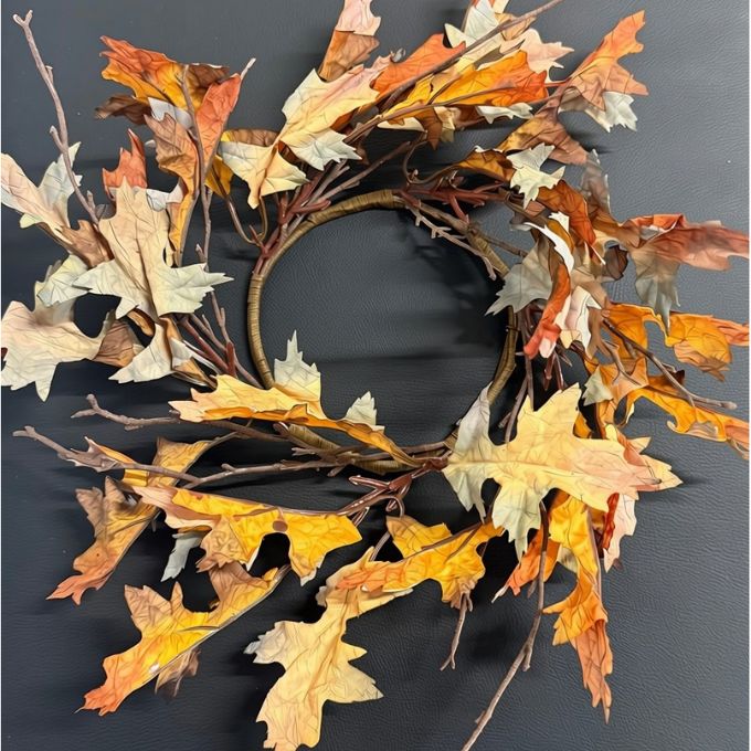 An autumn leaf wreath made of realistic oak leaves in shades of orange, yellow, brown, and beige, attached to a rustic brown branch base, displayed on a dark gray background. Candle Ring available at Quilted Cabin Home Parties in Airdrie