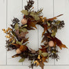 An autumn-themed artificial wreath with faux maple leaves in shades of brown, orange, and muted green, accented with small beige berries and dried pinecones, displayed against a white paneled background.  Maple and Pumpkin 6" ring available at  Quilted Cabin in Airdire
