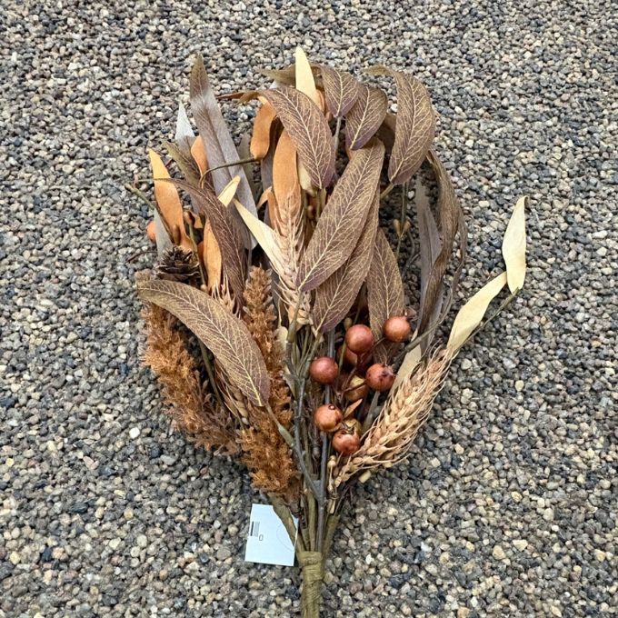 A dried botanical arrangement featuring brown and tan leaves, feathery stems, small pinecones, and clusters of brown berries, photographed on a gravel surface.  Available at Quilted Cabin in Airdrie