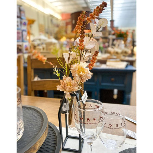 Decorative floral arrangement in a vase on a table with glasses in a blurred indoor setting. Brown and Tan Flower and White Eucalyptus Spray available at Quilted Cabin Home Decor.