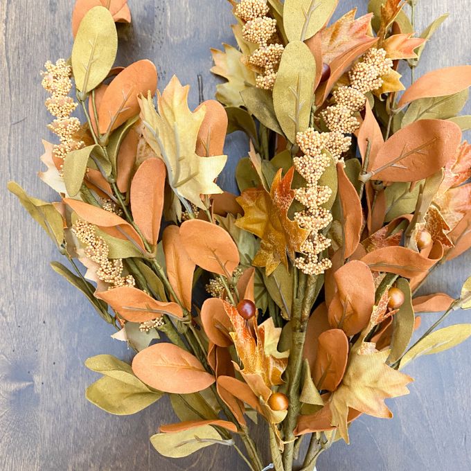 Autumn-themed wreath with leaves and berries on a wooden surface. Maple Leaf and Walking Fern Floral Spray available at Quilted Cabin Home Decor.