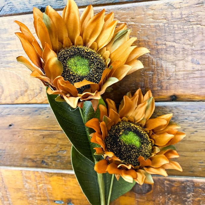 Two sunflowers on a wooden surface. Sunflower Sprays - Two Colours available at Quilted Cabin Home Decor.