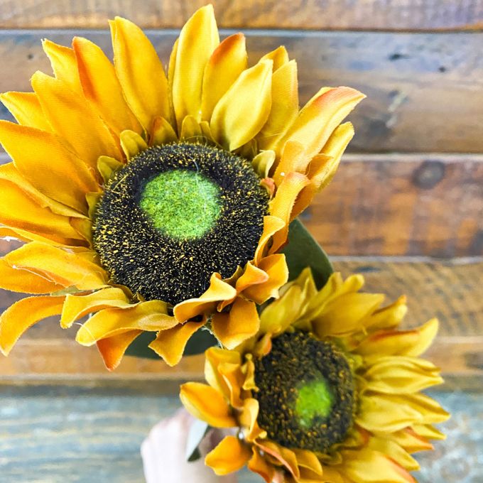 Two sunflowers with a wooden background. Sunflower Sprays - Two Colours available at Quilted Cabin Home Decor.
