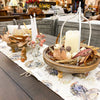 Decorative table setting with candles, pumpkins, and fall-themed centerpieces on a tablecloth. Pumpkin and Oak Leaf Candle Ring and Floral Spray available at Quilted Cabin Home Decor.
