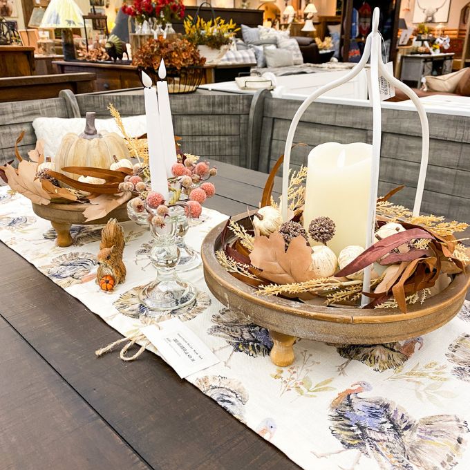 Decorative table setting with candles, pumpkins, and fall-themed centerpieces on a tablecloth. Pumpkin and Oak Leaf Candle Ring and Floral Spray available at Quilted Cabin Home Decor.