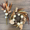 Decorative wreath with pumpkins and leaves on a wooden surface. Pumpkin and Oak Leaf Candle Ring and Floral Spray available at Quilted Cabin Home Decor.