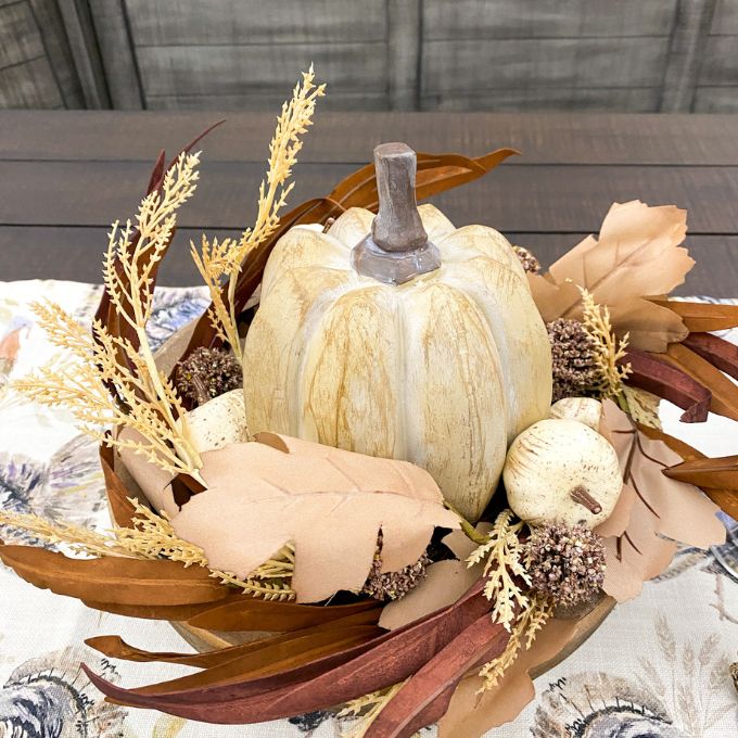 Decorative arrangement with pumpkins and fall foliage on a table. Pumpkin and Oak Leaf Candle Ring and Floral Spray available at Quilted Cabin Home Decor.