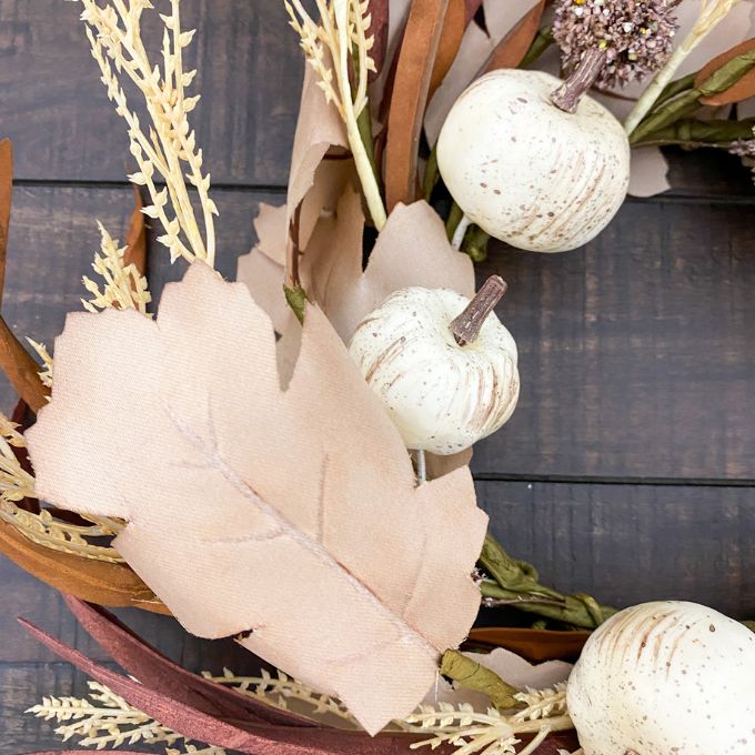 Decorative arrangement with white pumpkins and leaves on a wooden surface. Pumpkin and Oak Leaf Candle Ring and Floral Spray available at Quilted Cabin Home Decor.