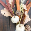 Decorative arrangement with white pumpkins, dried flowers, and ribbons on a dark wooden surface. Pumpkin and Oak Leaf Candle Ring and Floral Spray available at Quilted Cabin Home Decor.