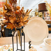 Decorative fall arrangement with leaves and pinecones in a vase, next to a white decorative plate. Earthy Maple Floral Spray available at Quilted Cabin Home Decor.