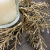 Gold glittery candle ring next to a candle on a dark surface. Golden Candle Ring/Small Wreath available at Quilted Cabin Home Decor.