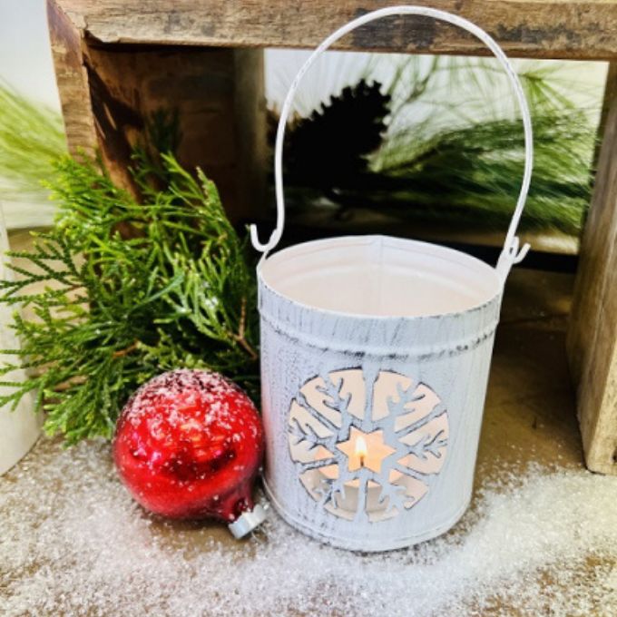 A white tin lantern with a snowflake cut out available at quilted cabin home decor.