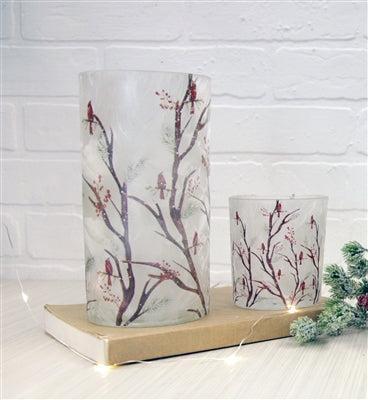 Two frosted glass candle holders with a bird and branch pattern, displayed on a book against a white brick wall background available at Quilted Cabin in Airdrie