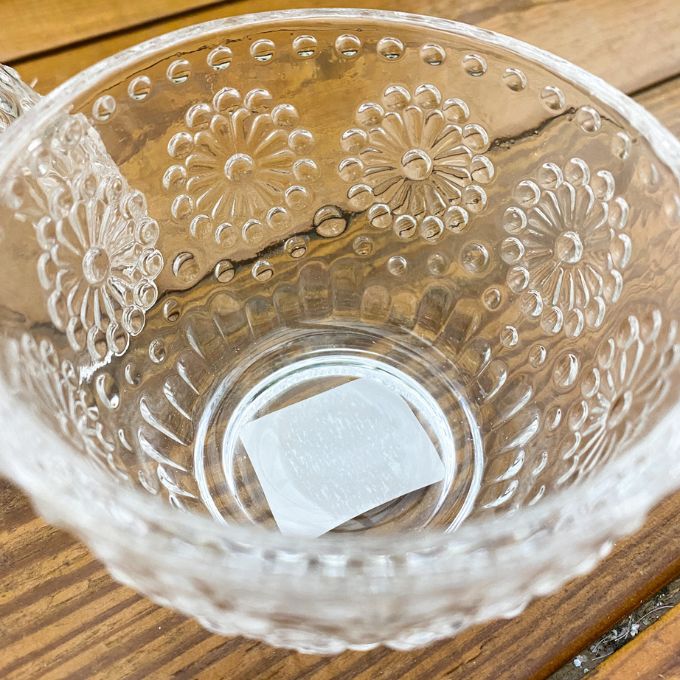 Clear glass bowl with floral embossing on a wooden surface.  Clear Glass Egg Shaped Dish with Bird Finial available at Quilted Cabin Home Decor.