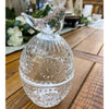Clear glass decorative item with bird on top on a wooden surface.  Clear Glass Egg Shaped Dish with Bird Finial available at Quilted Cabin Home Decor.