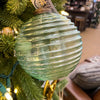Green ribbed glass ornament on a Christmas tree with blurred indoor background. Vintage Green Glass Ornaments - Three Styles available at Quilted Cabin Home Decor.