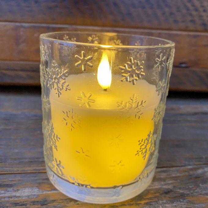 Candle in a glass holder with snowflake designs on a wooden surface. Snowflake Glass LED Timer Candle available at Quilted Cabin Home Decor.