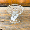 Clear glass candle holder on a wooden surface.  Simple Glass Candle Holder available at Quilted Cabin Home Decor.