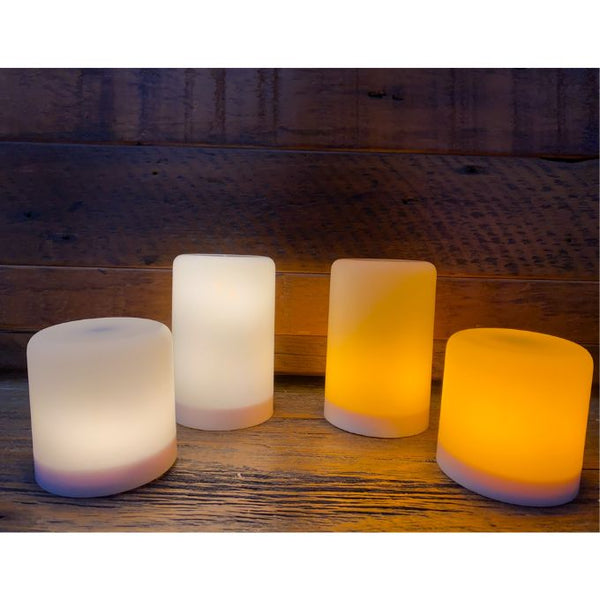 Set of four LED candles with different color temperatures on a wooden surface. Illusion Pillar LED Candles - Two Sizes and Colours available at Quilted Cabin Home Decor.