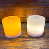 Two cylindrical LED lights, one orange and one white, on a wooden surface.  Illusion Pillar LED Candles - Two Sizes and Colours available at Quilted Cabin Home Decor.