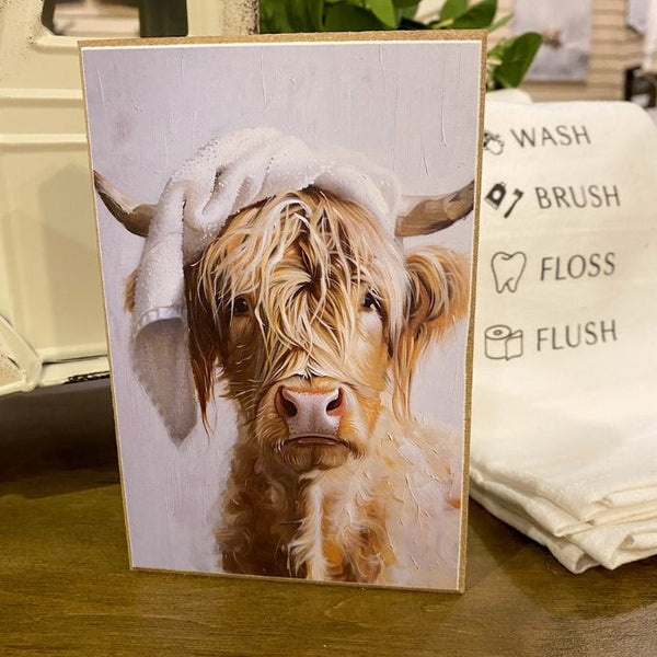 Card with a highland cow wearing a towel on its head, placed on a surface with a towel and text in the background. Just Washed Block Art available at Quilted Cabin Home Decor.