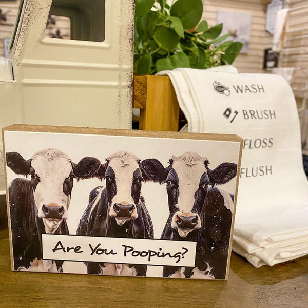 Block Sign with cow illustration and text 'Are You Pooping?' on a wooden surface. BAthroom Patrol Block Art available at Quilted Cabin Home Decor.