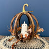 A decorative autumn pumpkin centerpiece with a rustic wooden ribbed frame, a small white ghost figurine in the center, and scattered brown and orange leaves around it, set against a blue wall. Ghost candle available at Quilted Cabin in Airdrie
