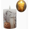 A Halloween-themed flameless LED pillar candle with a white ghost, jack-o'-lantern, and full moon design on a gray background, shown alongside an inset image of the candle glowing with a warm yellow light.  Available at Quilted Cabin in Airdrie