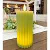 Green Ridged candle on a wooden surface with a blurred indoor background.  Sage Green Ridged LED Pillar Timer Candle available at Quilted Cabin Home Decor.