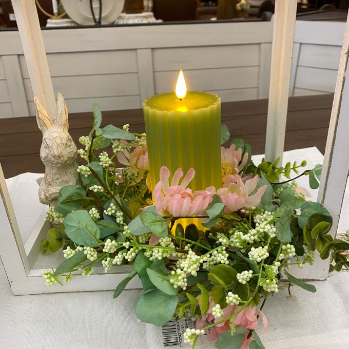 Decorative arrangement with a lit candle, flowers, and greenery in a white holder. Sage Green Ridged LED Pillar Timer Candle available at Quilted Cabin Home Decor.
