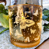 Glass candle holder with butterfly designs on a textured surface.  Golden Butterfly Glass Jar LED Timer Candle available at Quilted Cabin Home Decor.