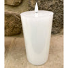 White candle on a stone surface with a stone wall background. White LED Timer Pillar Candles - Three Sizes available at Quilted Cabin Home Decor.