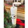 White candle shaped like a snowman on a table with Christmas decorations. Snowman LED Taper Timer Candle available at Quilted Cabin Home Decor.
