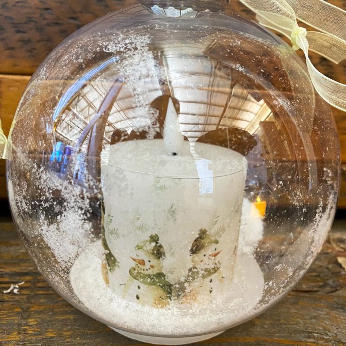 Decorative glass ball with a candle and snowman inside on a wooden surface. Ball Ornaments with LED Candles - Three Styles available at Quilted Cabin Home Decor.