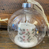 Decorative candle in a glass ball with a yellow ribbon on a wooden surface. Ball Ornaments with LED Candles - Three Styles available at Quilted Cabin Home Decor.