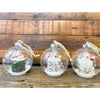 Three clear glass ball ornaments with candles inside on a wooden surface. Ball Ornaments with LED Candles - Three Styles available at Quilted Cabin Home Decor.